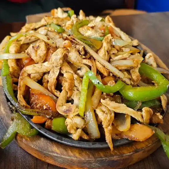 Large sizzling chicken fajita platter with bell peppers and onions